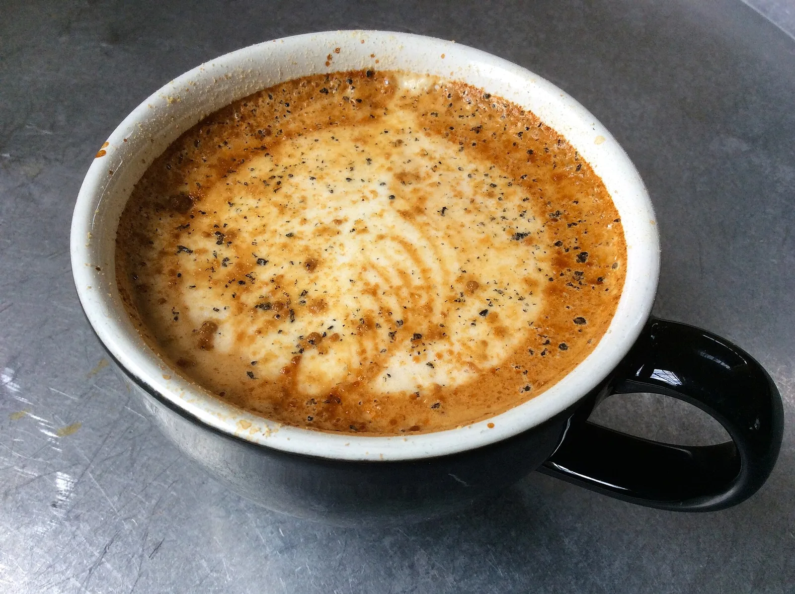 A latte in a black cup on a metal cafe table at a coffee shop in Durham. The photo was not taken in Cary.