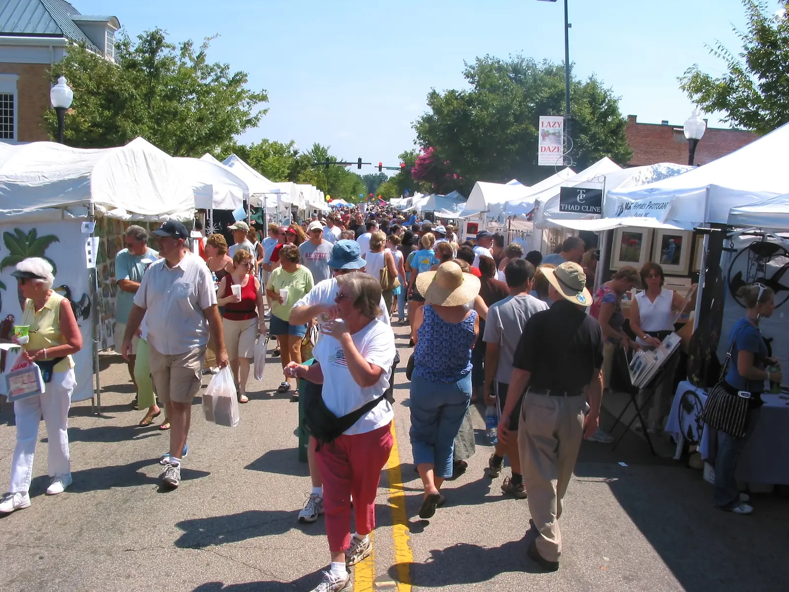 Crowds walk between artist tents under a Lazy Daze banner on a closed street in downtown Cary.