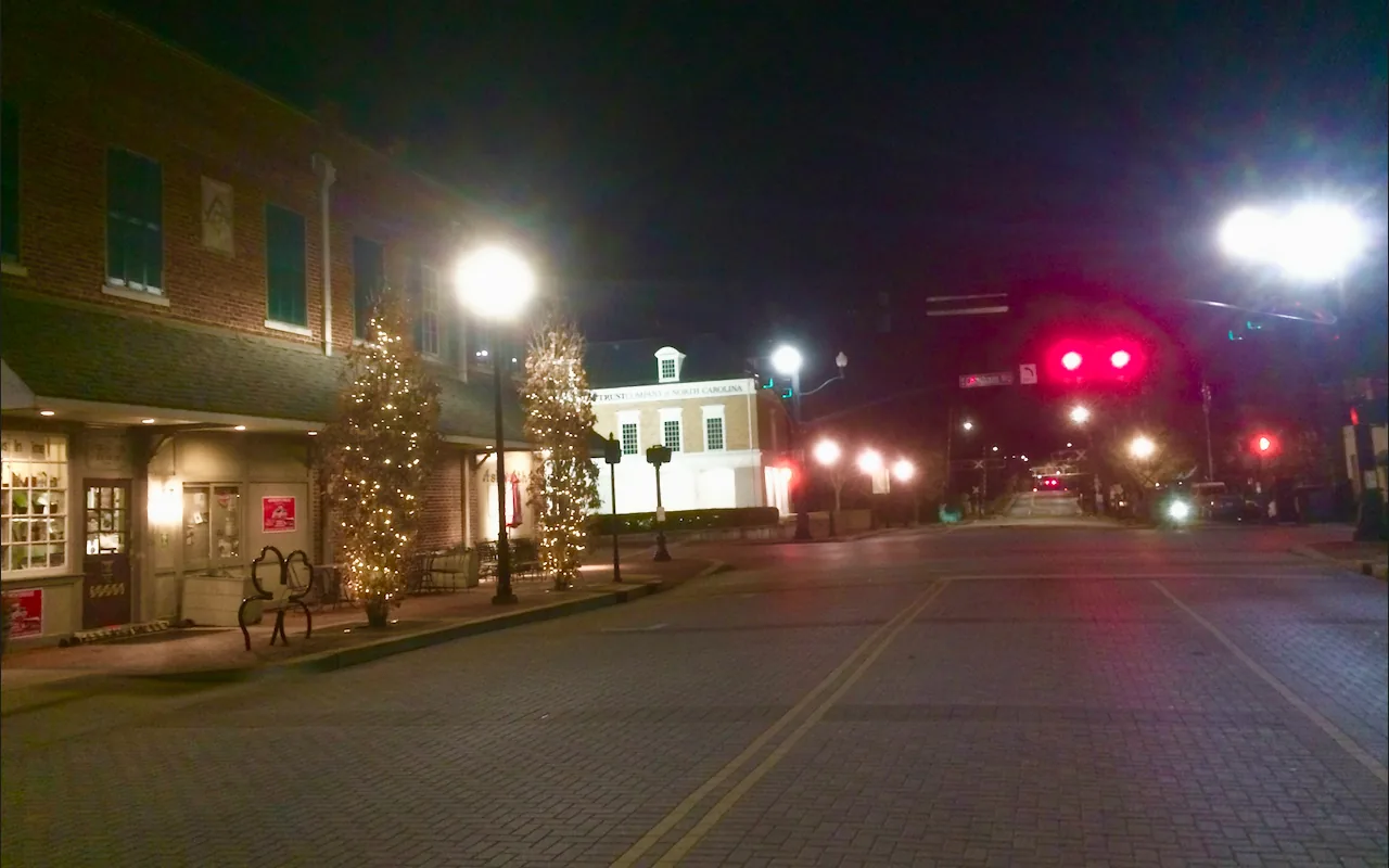 Storefronts and lighted trees along a brick street in downtown Cary at night