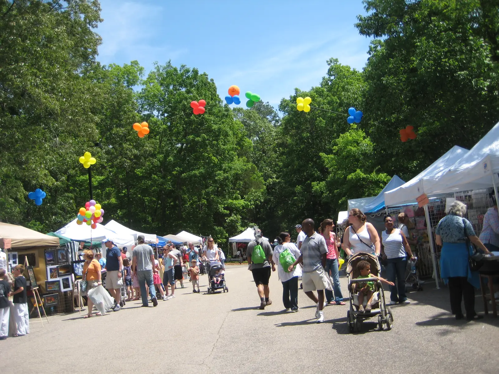 Visitors walk past artist tents along a park road at the Spring Daze Arts and Crafts Festival in Bond Park, Cary.