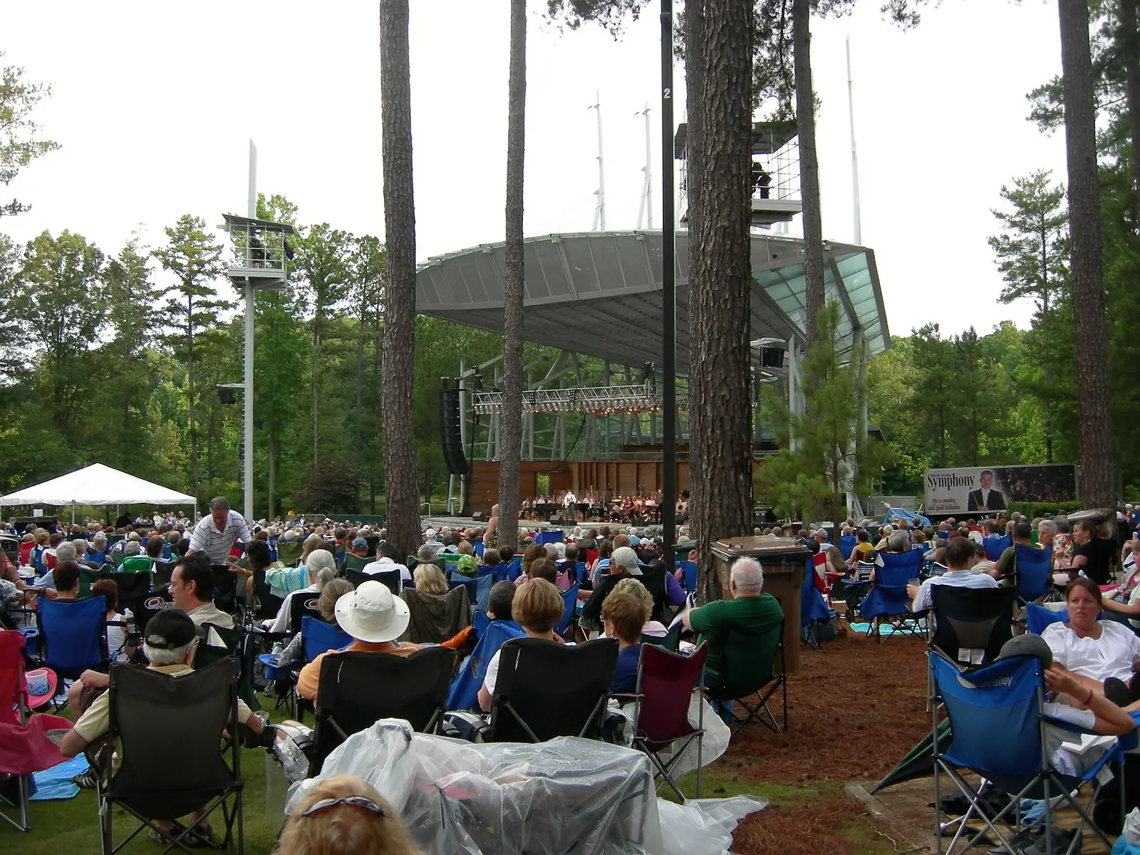 Concertgoers in lawn chairs fill the tree-shaded lawn in front of the stage at Koka Booth Amphitheatre in Cary.