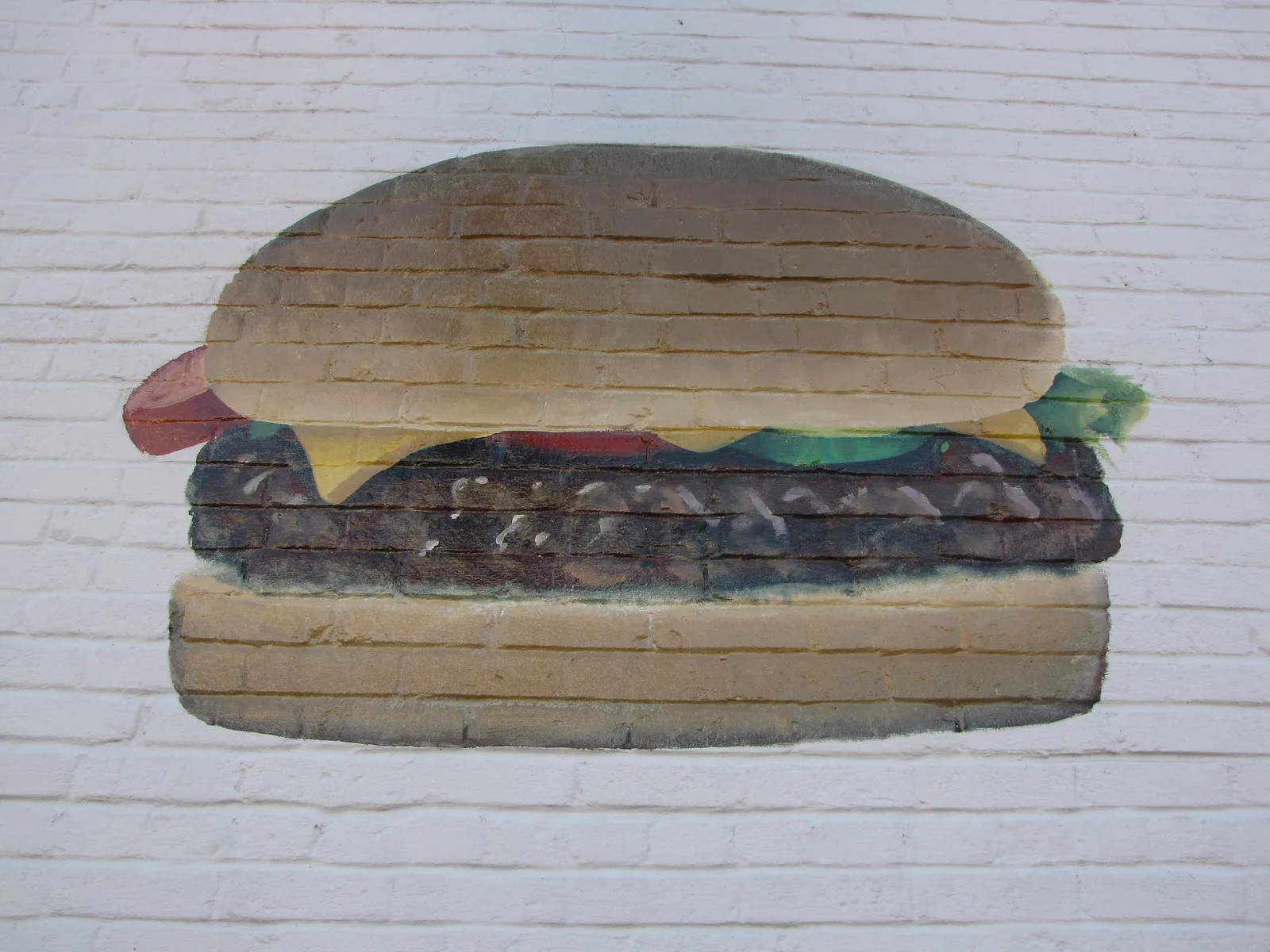 A cheeseburger painted on a white brick wall. The mural is not in Cary.